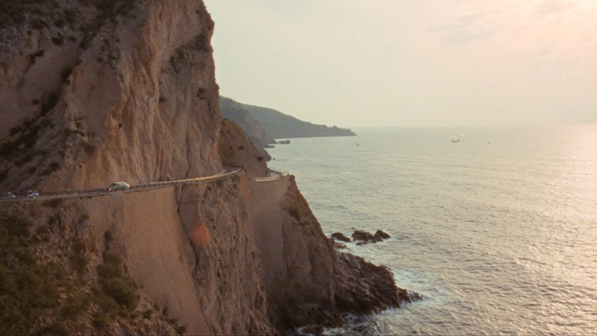 A coastal road winding along cliffs above the sea at golden hour, shot on film